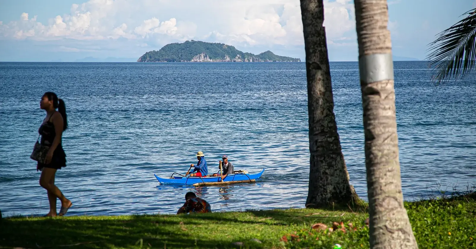 Local boatmen paddling an outrigger banca off the shore in Dauin, Negros Oriental, with an island visible on the horizon